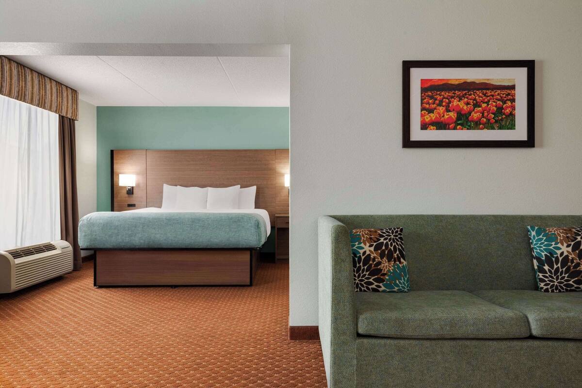 Une chambre d’hôtel avec un lit, un canapé, un tableau accroché au mur et une fenêtre avec des rideaux.