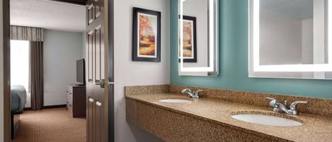 A hotel bathroom with two sinks, a large mirror, and artwork on the wall.