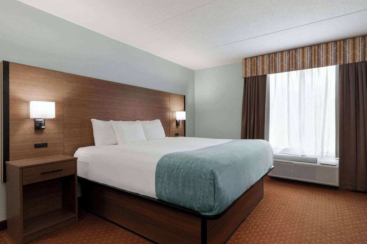 Une chambre d’hôtel avec un grand lit, deux tables de chevet avec des lampes, une fenêtre avec des rideaux et un climatiseur fixé au mur.