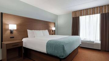 A hotel room with a large bed, two bedside tables with lamps, a window with curtains, and a wall-mounted air conditioning unit.