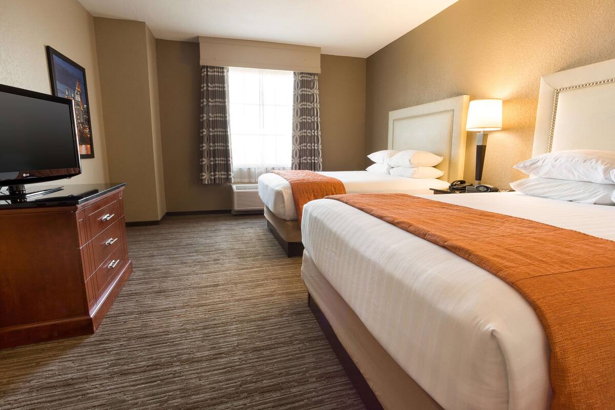 A hotel room with two beds, a television, a desk, and a window with curtains.