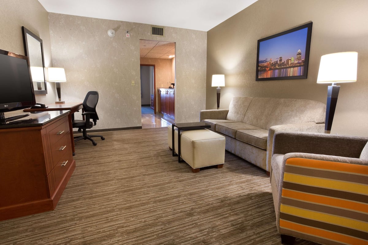 A hotel room with a desk, office chair, sofa, ottoman, and a television.