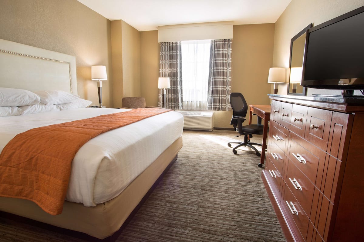 A hotel room with a large bed, a desk with a chair, a television, and a dresser.