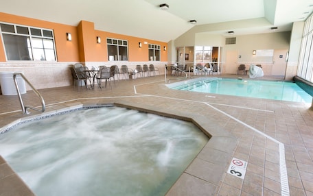 An indoor swimming pool area with a hot tub, lounge chairs, and a tiled floor.