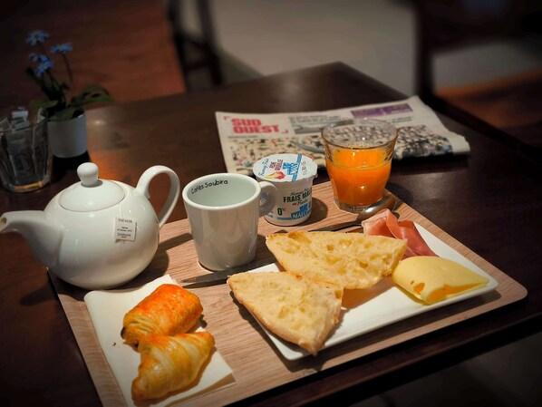Bandeja de desayuno con croissants, queso, jamón, tetera, taza, vaso de zumo de naranja y recipiente de yogur.