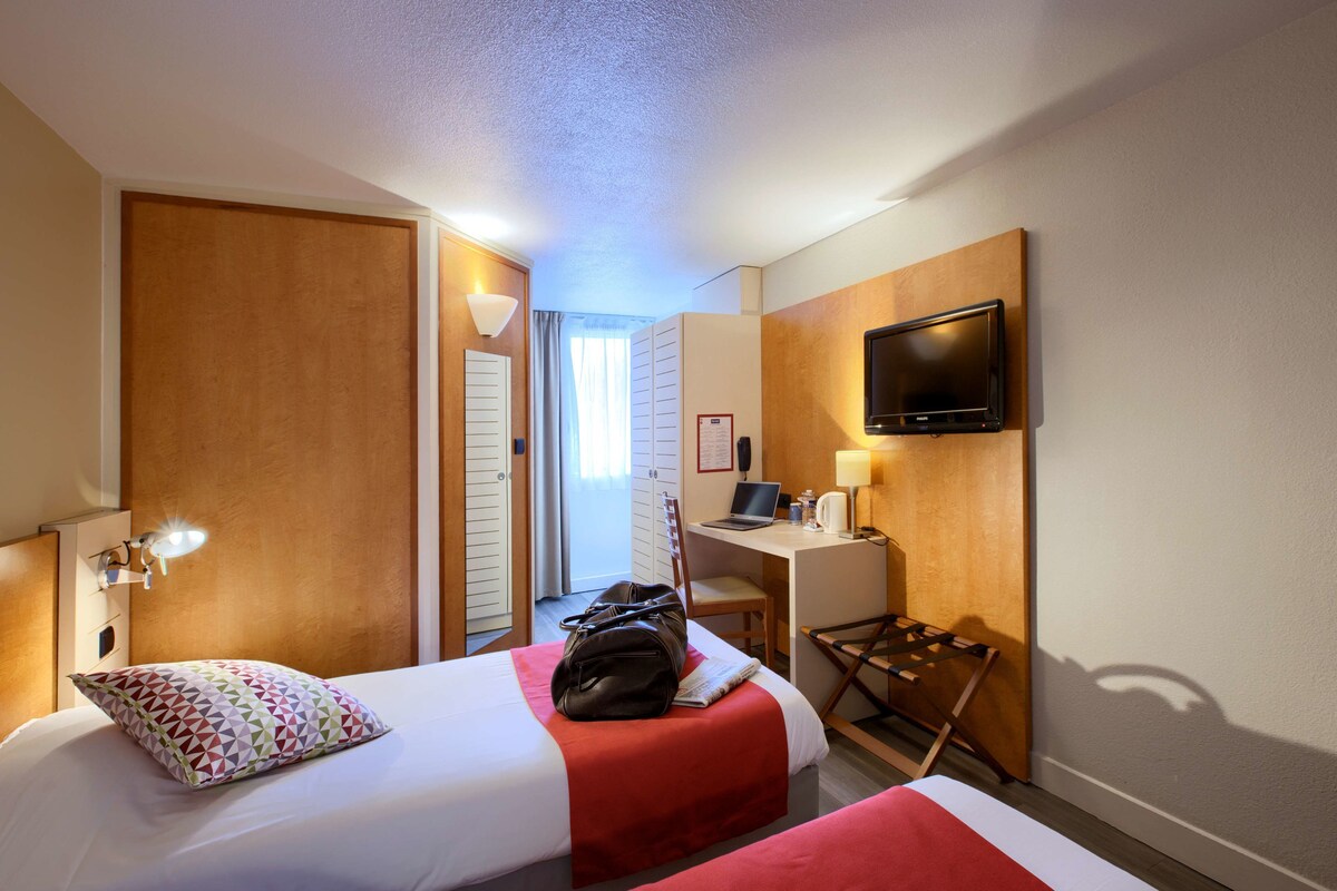 Habitación de hotel con dos camas, un escritorio, un televisor y un armario.