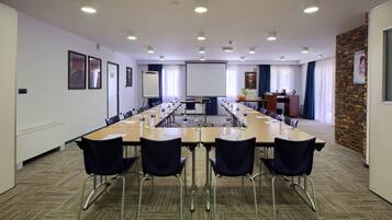 A conference room with a long table, chairs, a projector screen, and a brick accent wall.