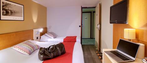 Una habitación de hotel con dos camas, un escritorio con una computadora portátil, un televisor y una puerta que da a otra habitación.