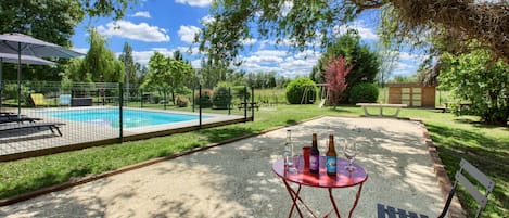 A backyard with a swimming pool, a table with bottles and glasses, and a bench.