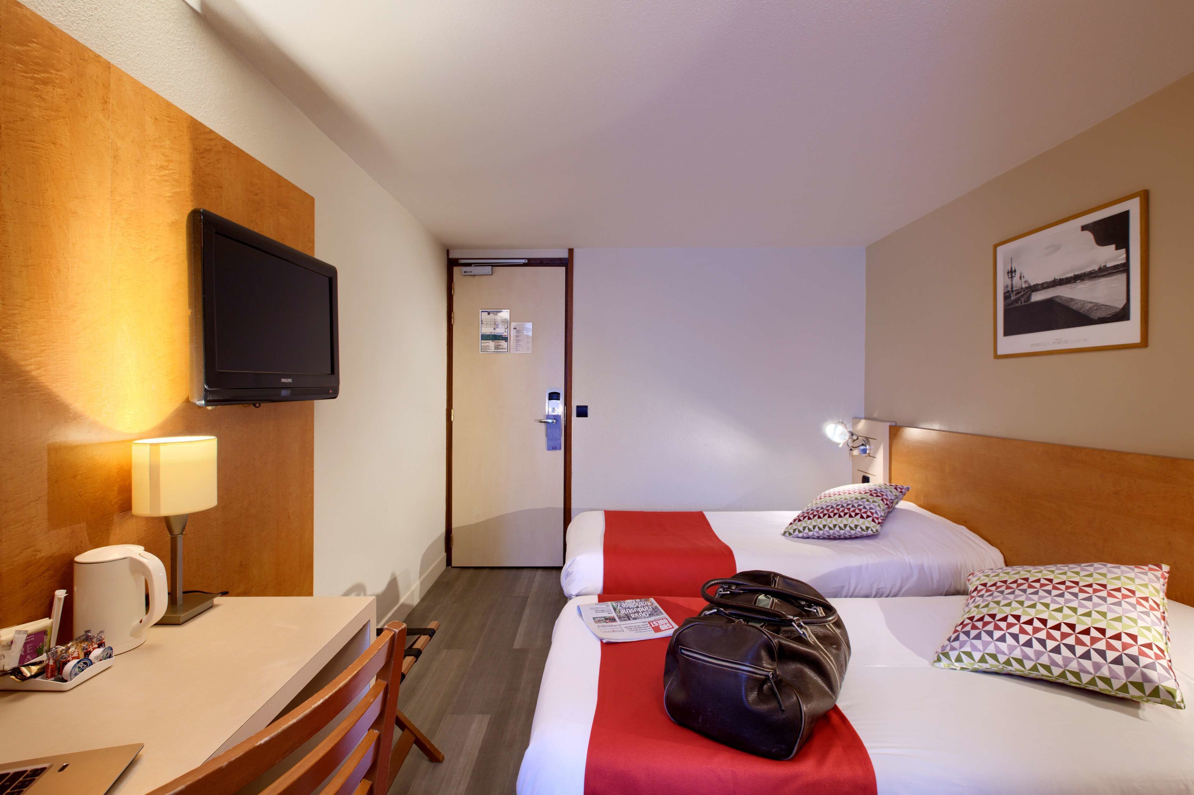 Una habitación de hotel con cama, escritorio, televisor y puerta.