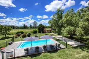 Un patio trasero con piscina, rodeado de una valla, y equipado con sillas de descanso y sombrillas.