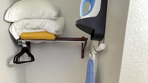 A corner of a room with a bed, a hanging iron, and a blue ironing board.