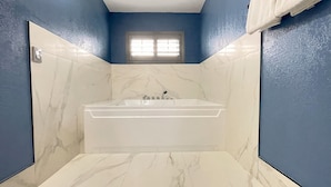 A bathroom with a bathtub, white marble tiles, and blue walls.