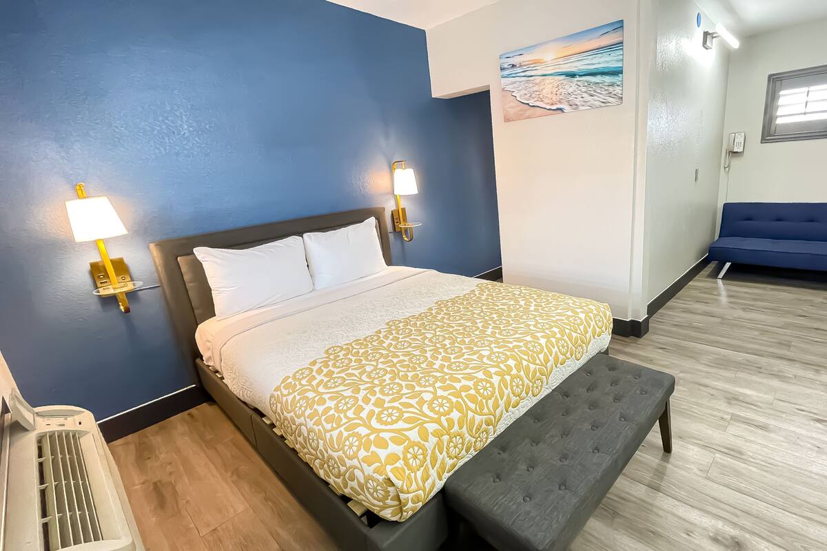 A hotel room with a bed, bedside lamps, a painting, a blue sofa, and a desk.