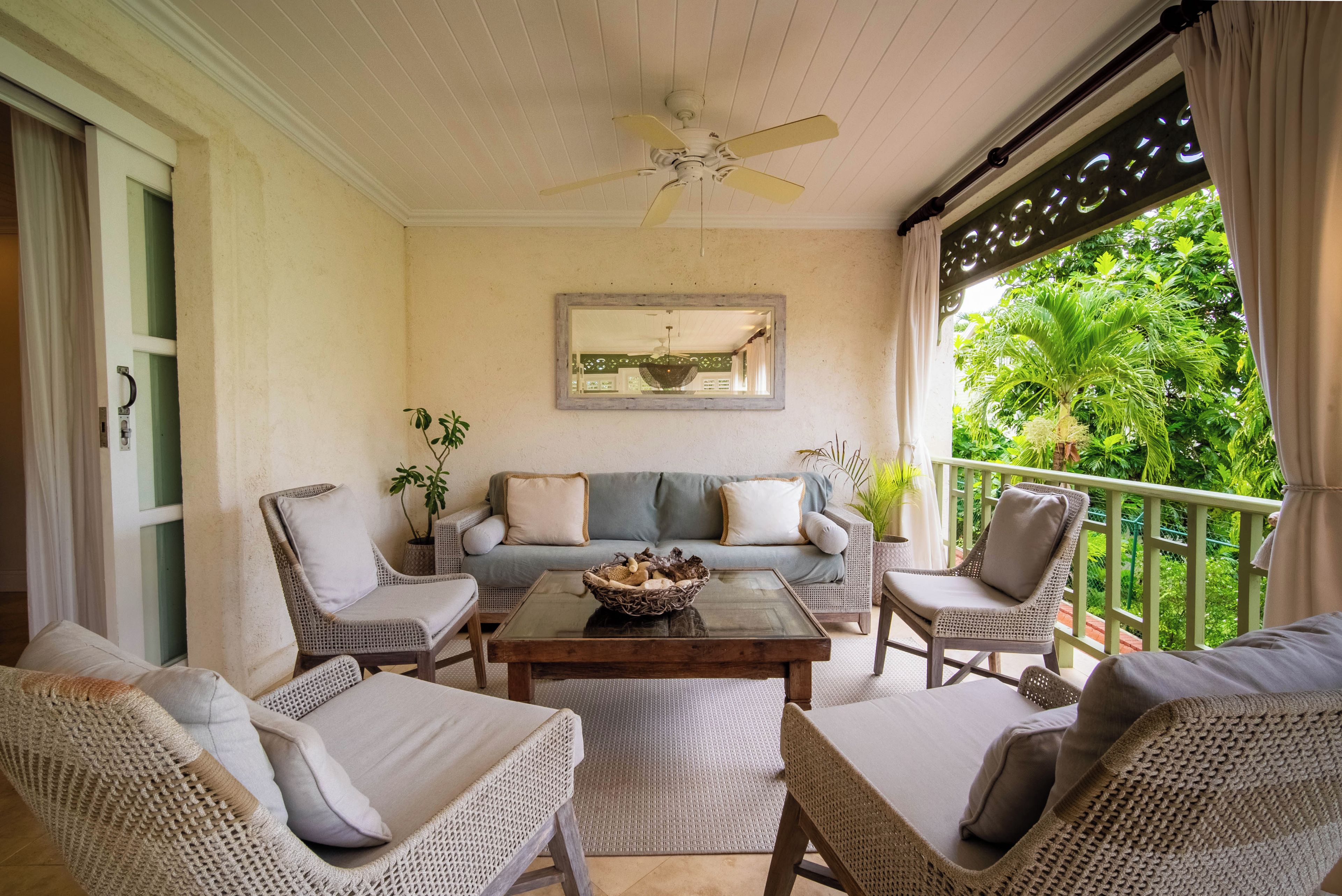 A balcony with wicker furniture, a ceiling fan, and a view of lush greenery.