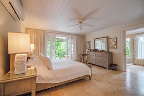 A bedroom with a bed, a nightstand, a dresser, a ceiling fan, and a window with curtains. - Little Good Harbour (Speightstown)