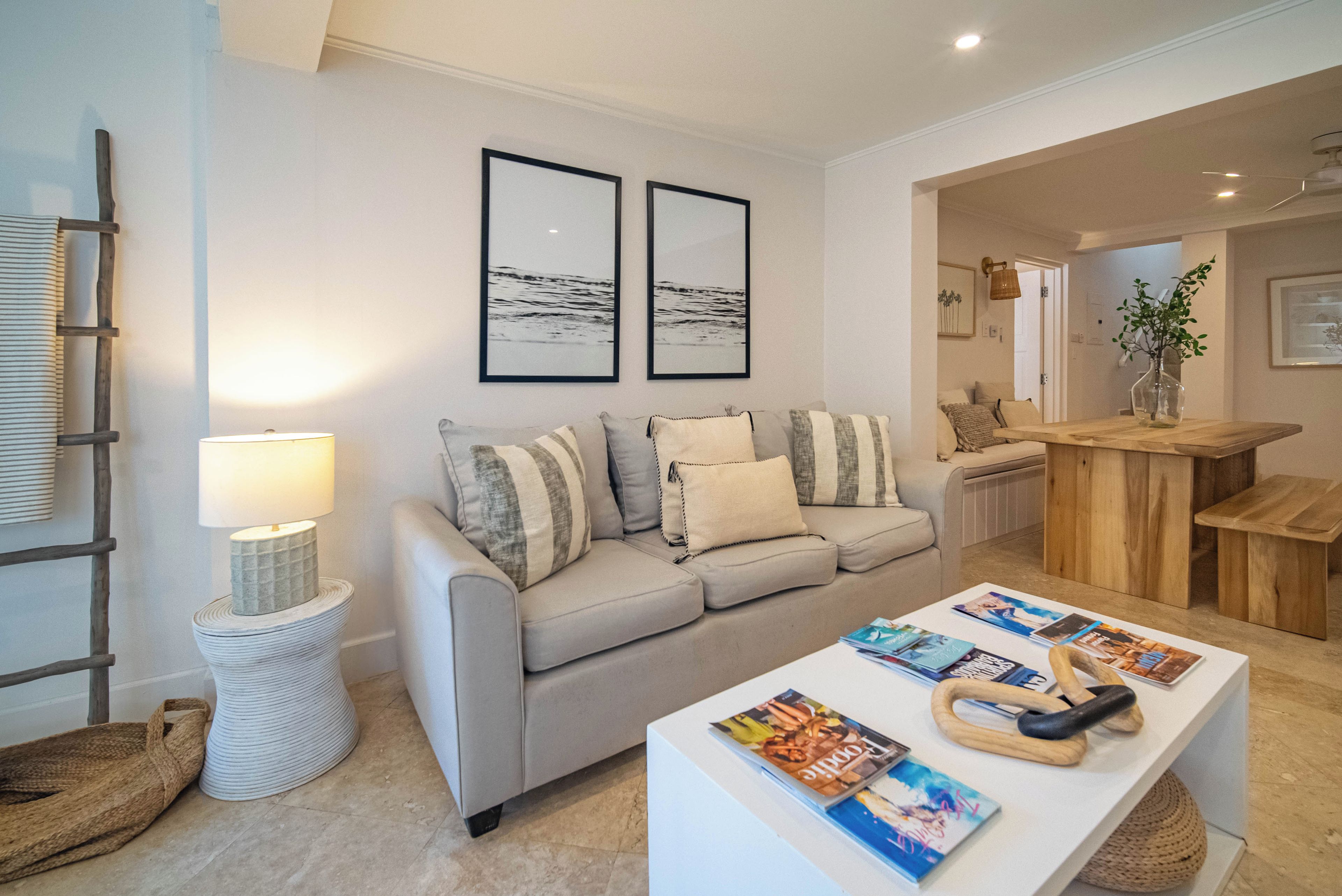 A modern living room with a sofa, a coffee table with magazines, a lamp, and two framed pictures on the wall.