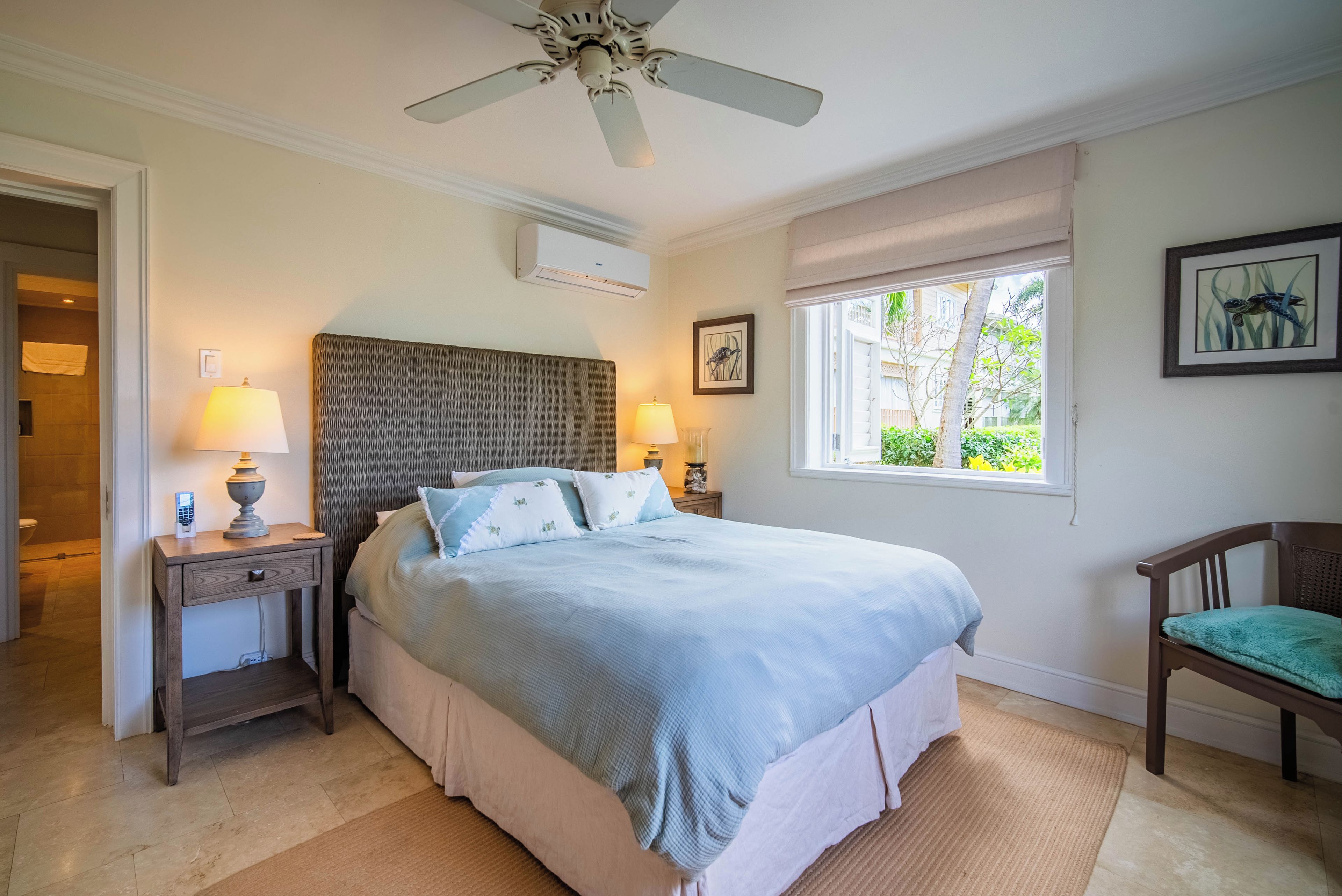 A bedroom with a bed, bedside lamps, a ceiling fan, a window with a view, and a chair.