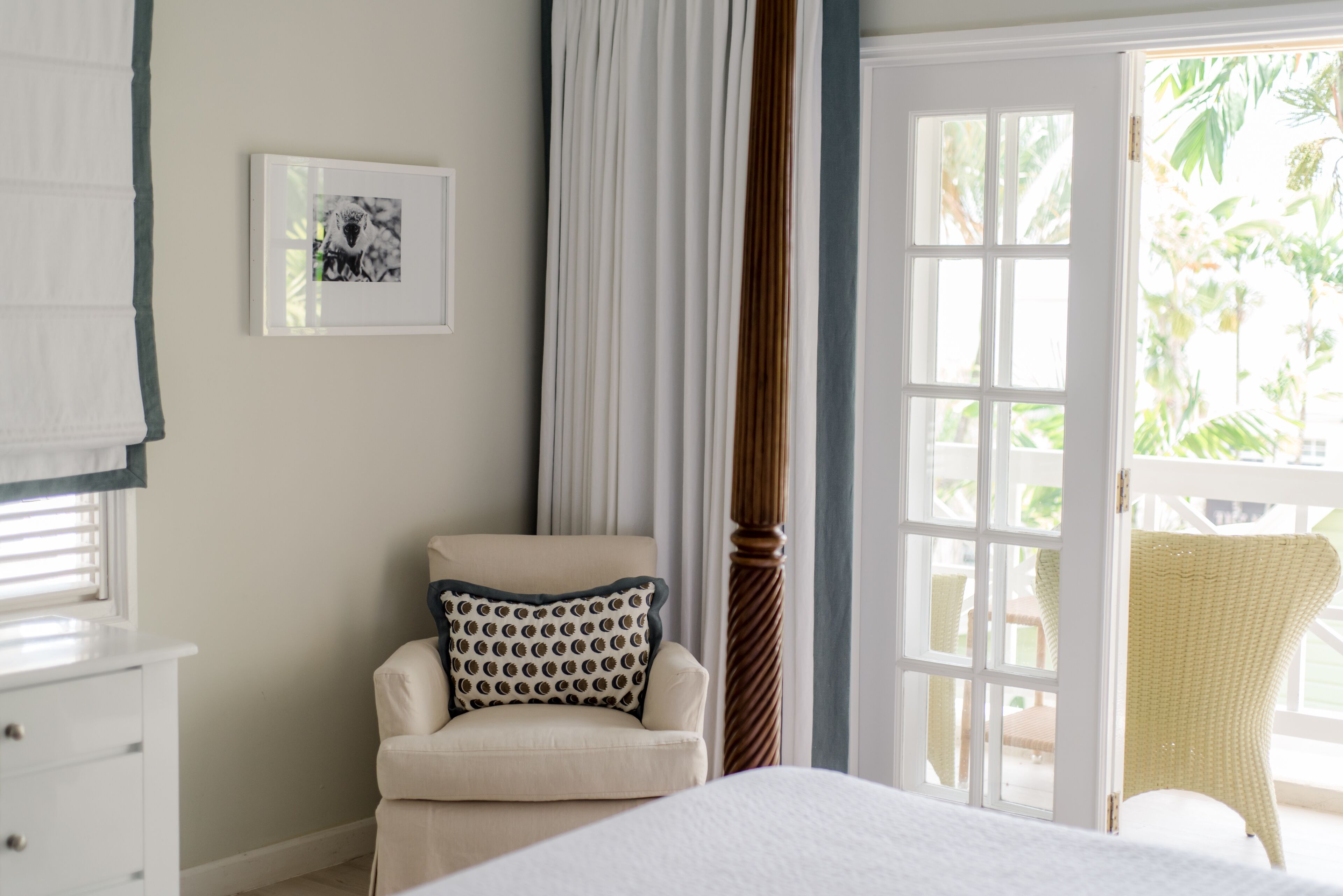 A bedroom with a bed, a chair, a bedside table, a window with curtains, and a door leading to an outdoor area.
