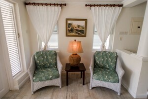 Una habitación con dos sillones de mimbre con cojines estampados, una mesita con una lámpara y un cuadro en la pared.