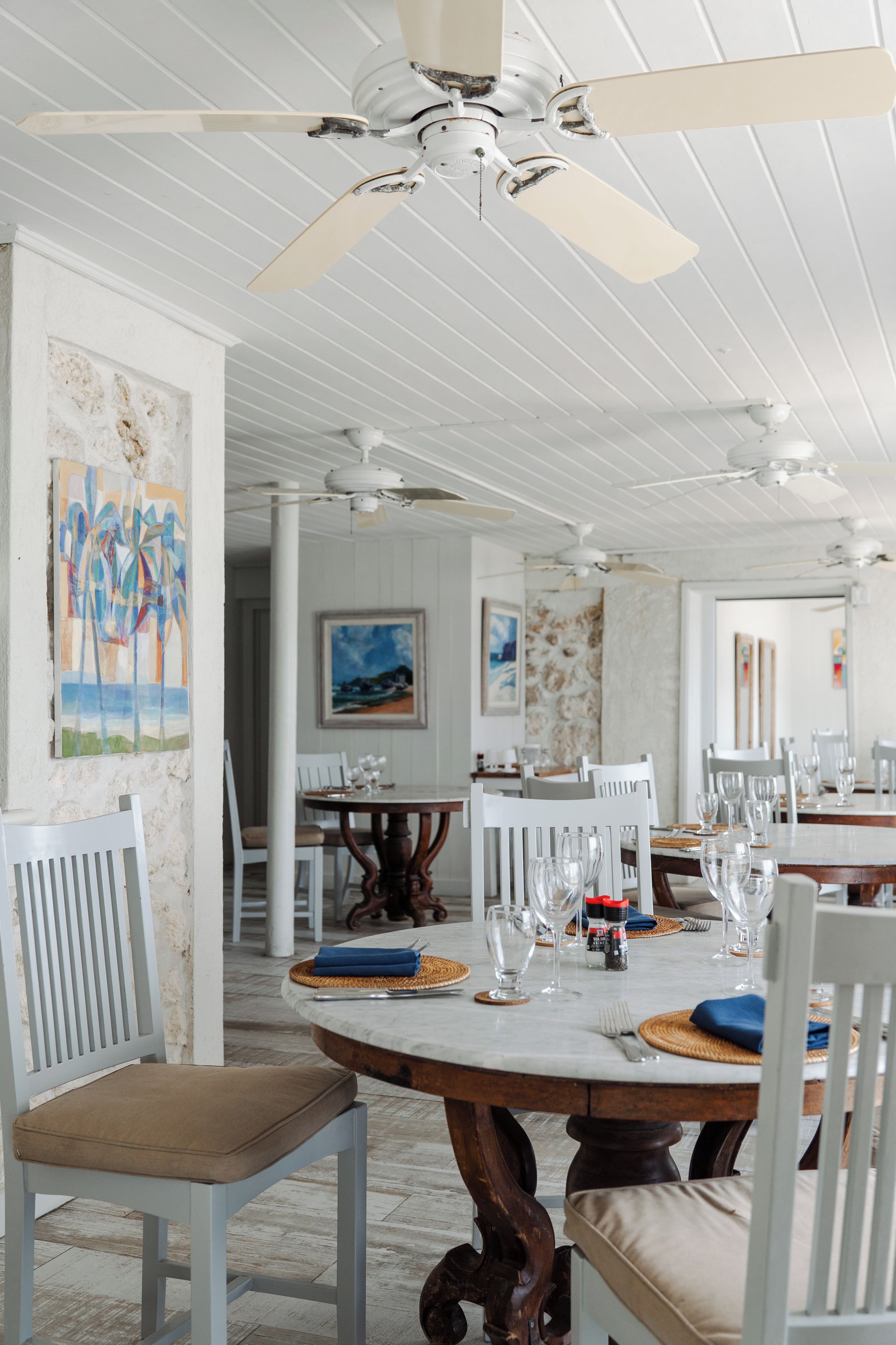 A dining area with white wooden chairs, a marble table, and ceiling fans.