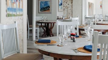 Un comedor con sillas de madera blanca, una mesa de mármol y ventiladores de techo.