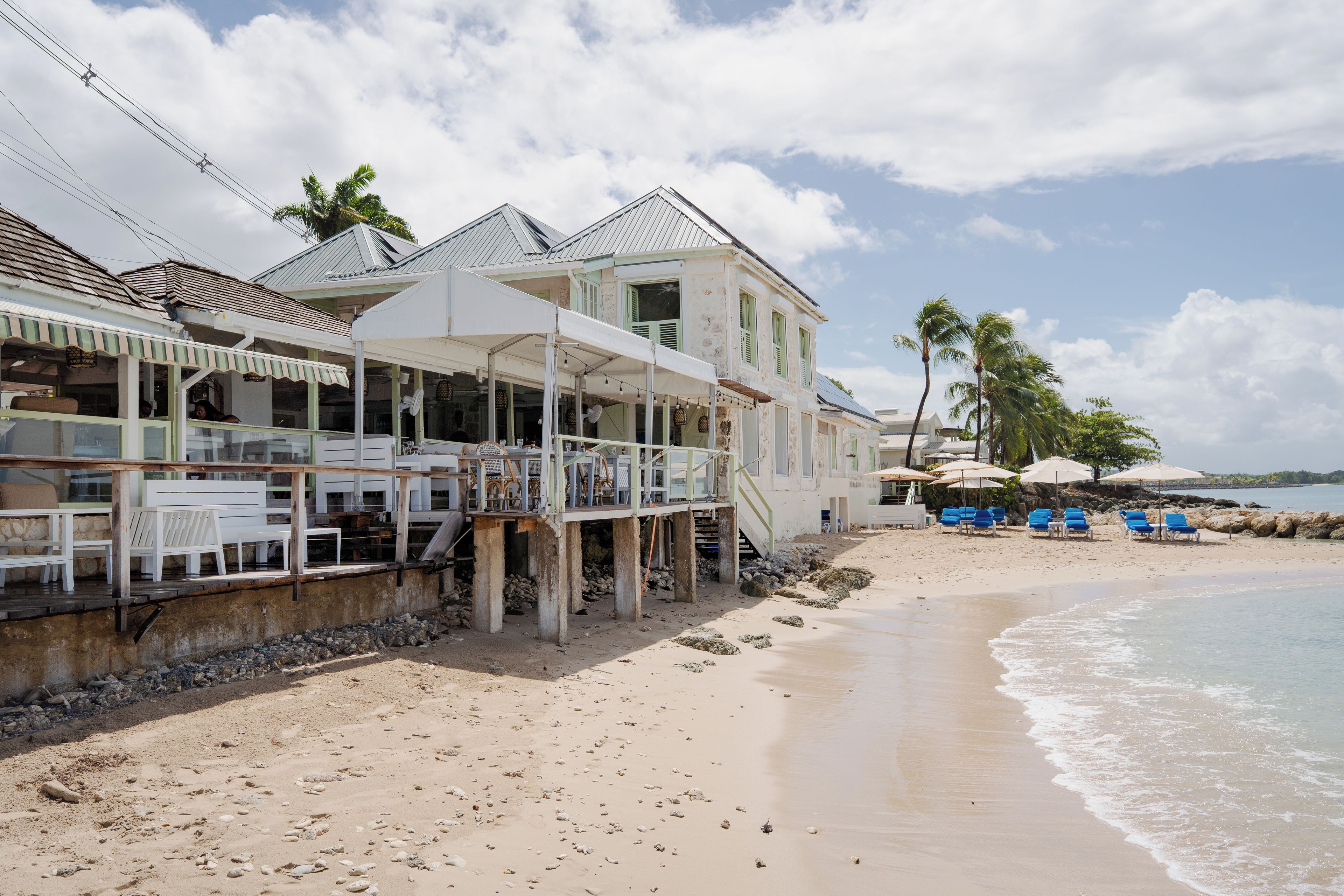 Une propriété située en bord de mer, dotée d’un espace repas, de plusieurs pièces et d’une plage avec des parasols et des chaises longues.