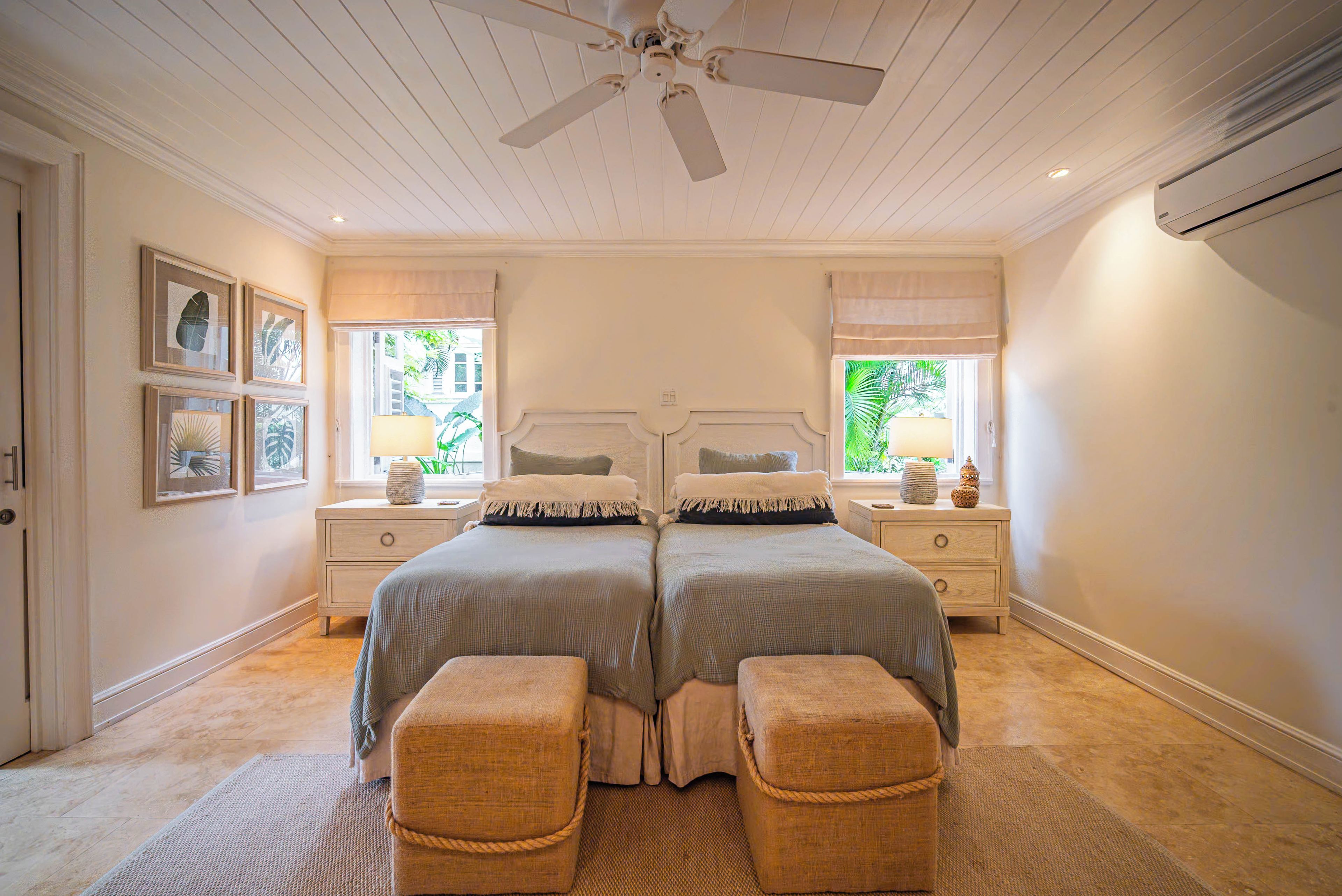 Une chambre avec deux lits, un ventilateur de plafond et une fenêtre donnant sur un paysage verdoyant.