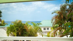 A balcony with wicker furniture overlooking a pool and a view of the ocean. - Little Good Harbour (Speightstown)