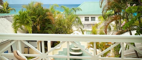A balcony with wicker furniture overlooking a pool and a view of the ocean.
