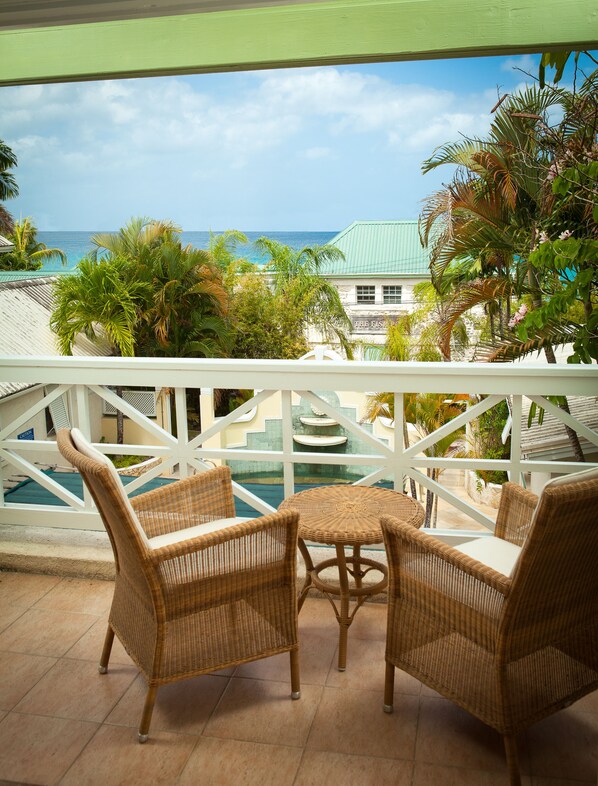 A balcony with wicker furniture overlooking a pool and a view of the ocean. - Little Good Harbour (Speightstown)