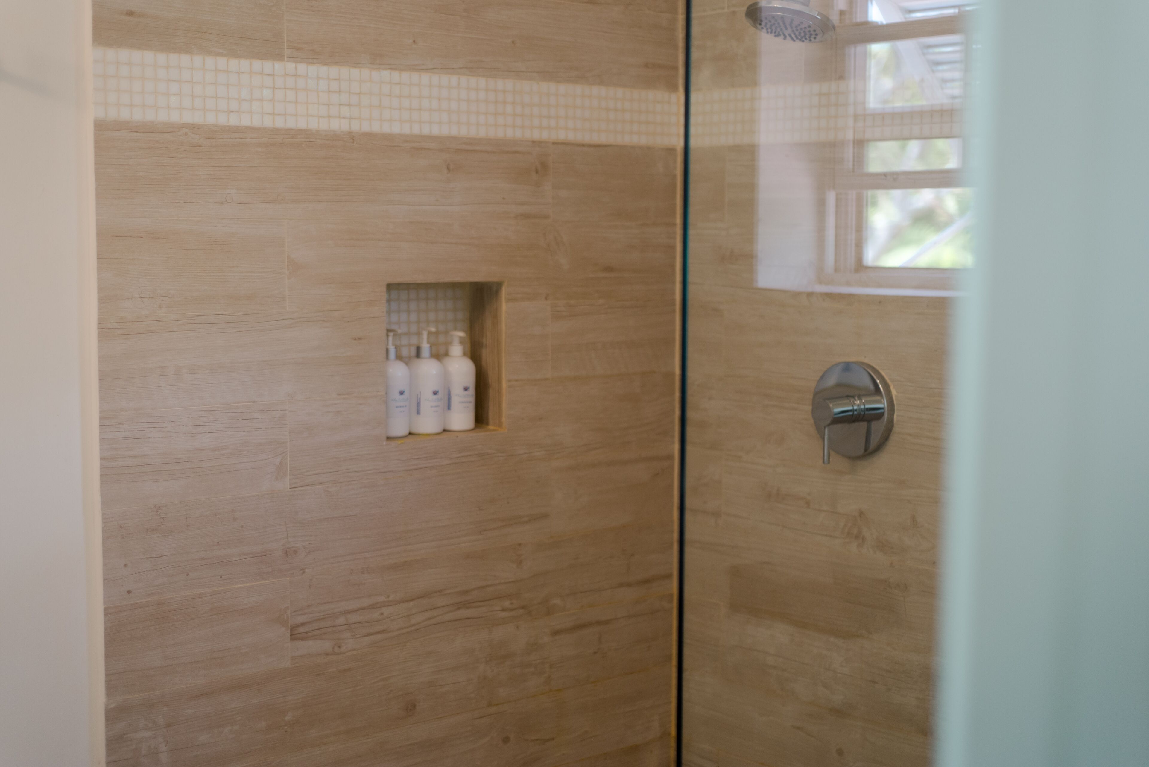 Zona de ducha con paredes de madera, una puerta de cristal y un estante pequeño con artículos de aseo.
