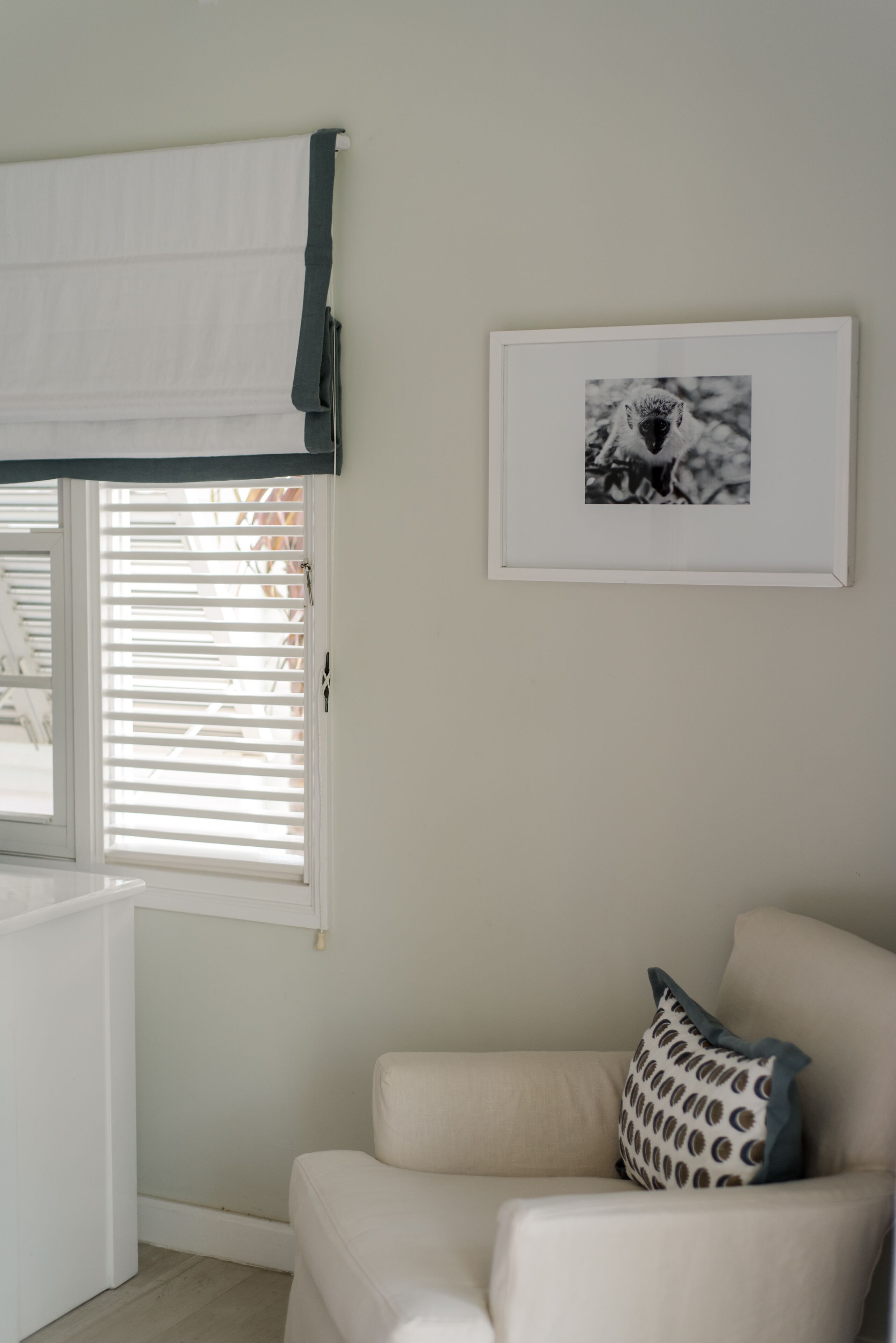 A room with a white sofa, a framed picture on the wall, and a window with blinds.