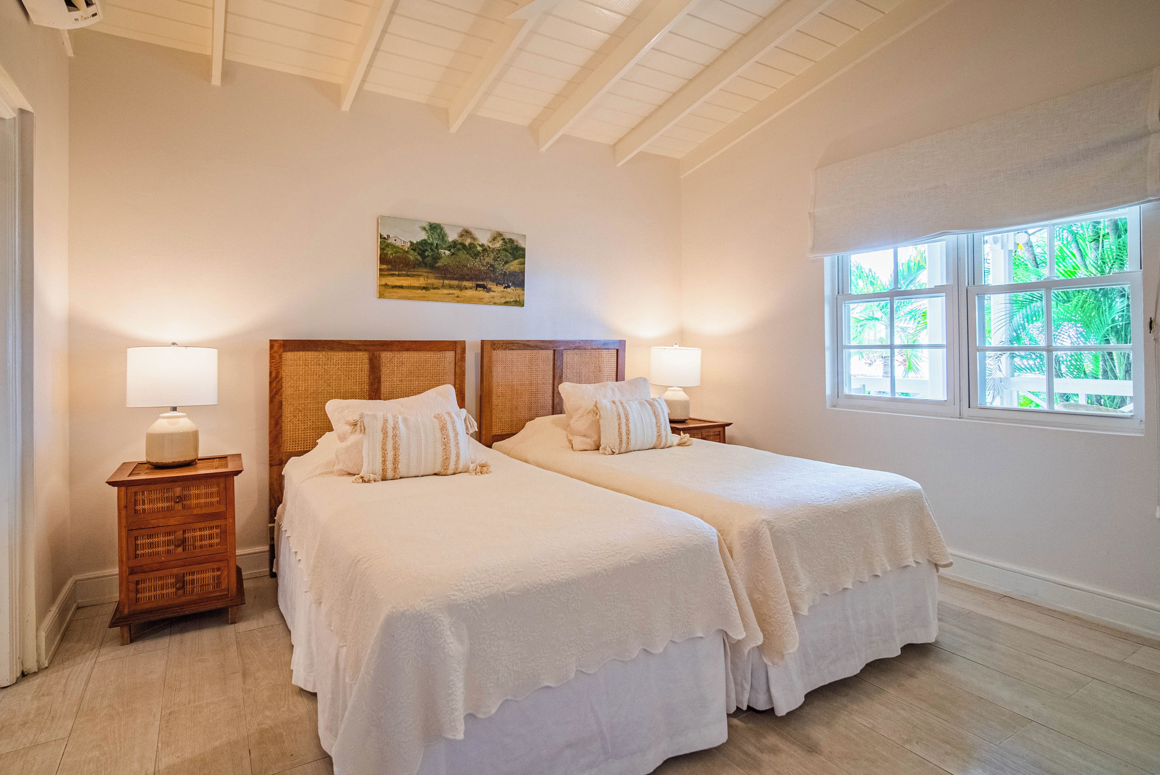 Un dormitorio con dos camas, cabeceros de madera, lámparas de noche, un cuadro en la pared y una ventana con vistas a zonas verdes.