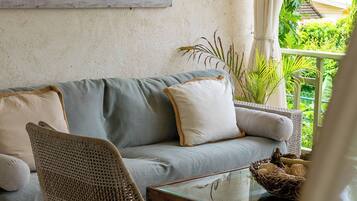A cozy living area with a sofa, a wicker chair, a glass coffee table, and a view of greenery outside.