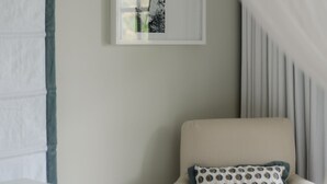 A room with a white armchair, a framed picture on the wall, and a sheer curtain. - Little Good Harbour (Speightstown)