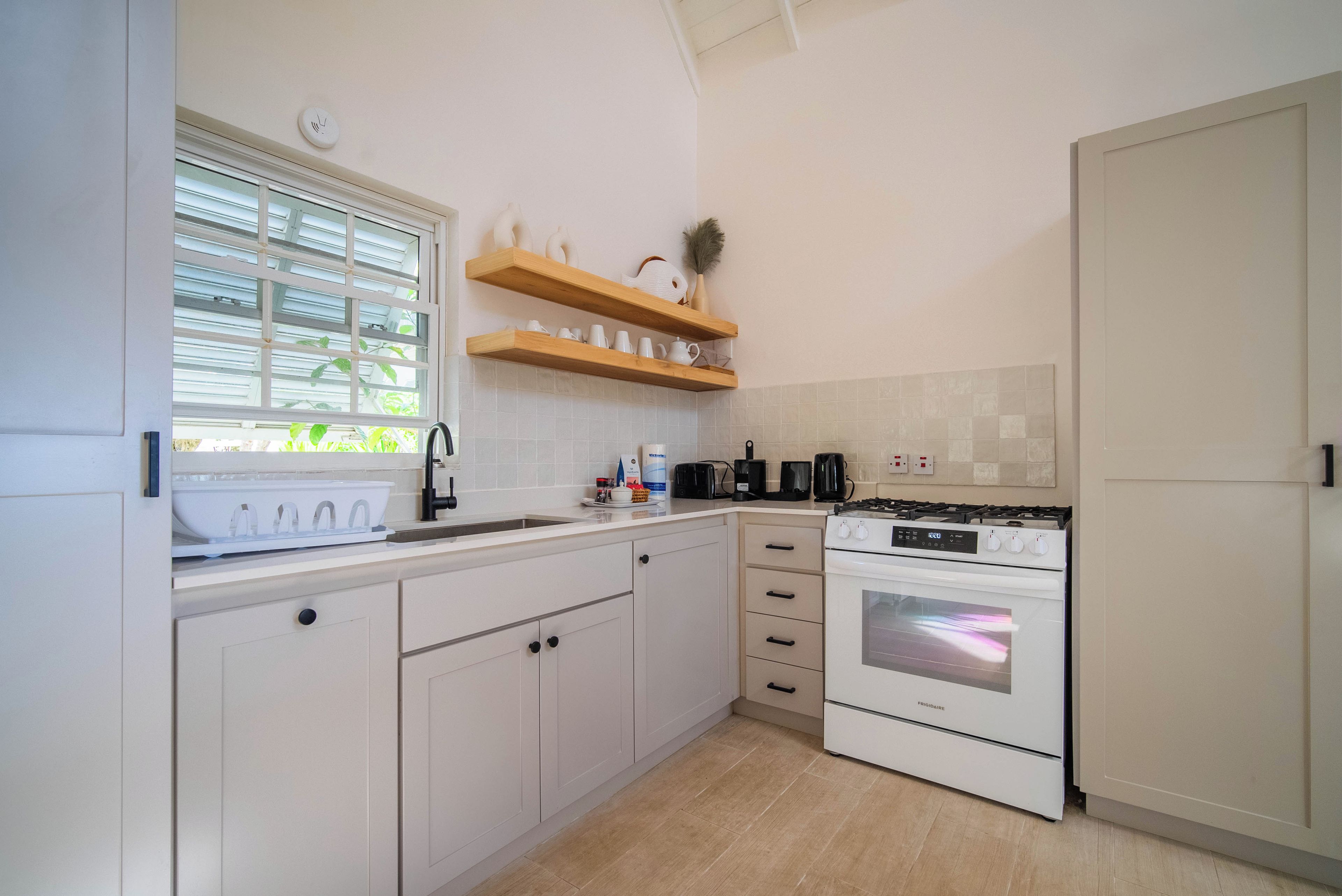 A kitchen with white cabinets, a stove, and a window with blinds.