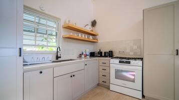 A kitchen with white cabinets, a stove, and a window with blinds.