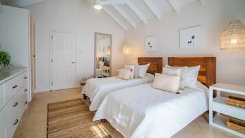 Ein Schlafzimmer mit zwei Betten, einem Holzkopfstück, einer weißen Kommode, einem gewebten Teppich und einem Deckenventilator.