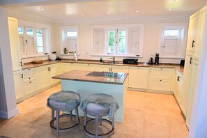 A spacious kitchen with white cabinetry, a granite countertop, and two bar stools. - Little Good Harbour (Speightstown)