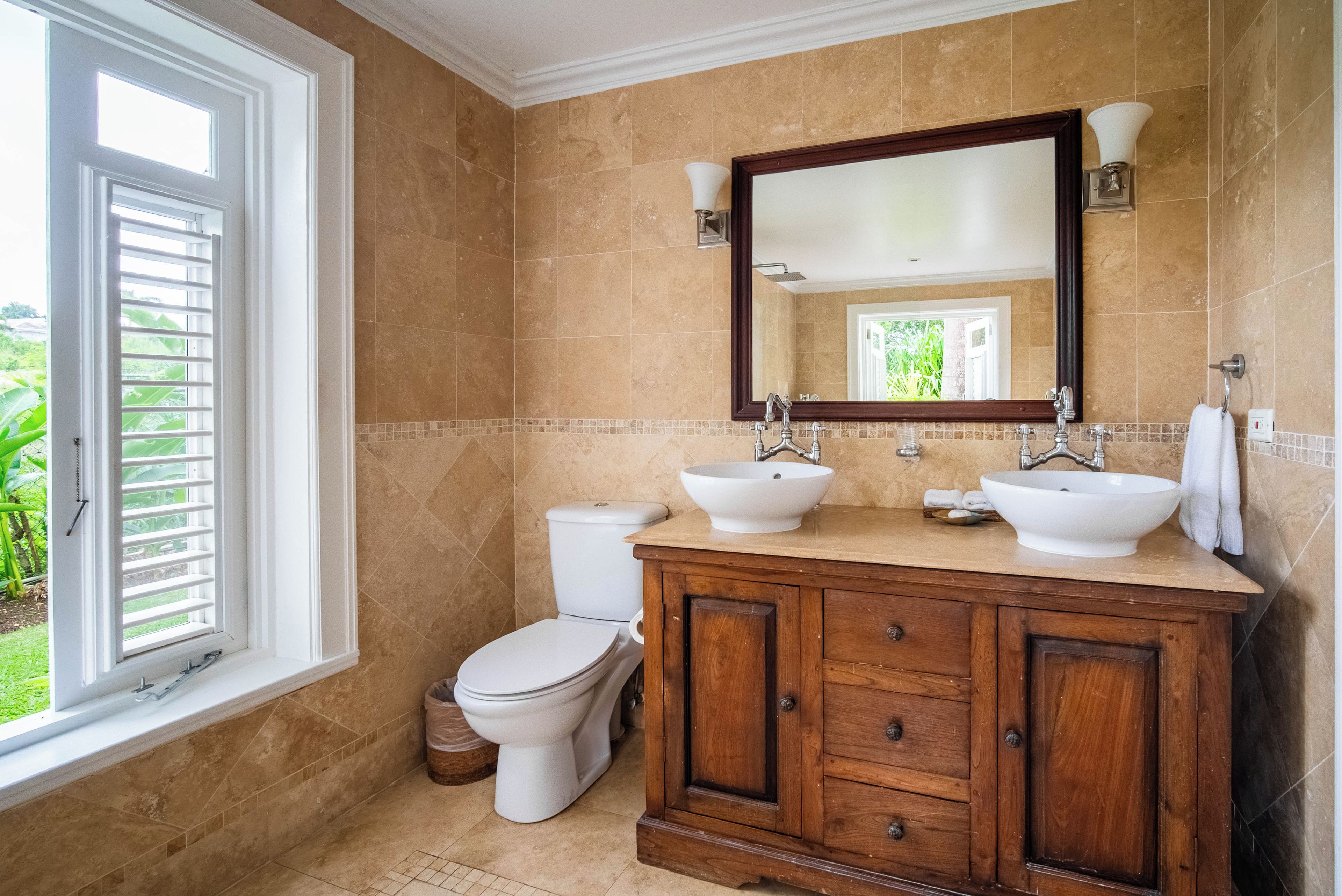 Une salle de bain avec deux lavabos, des toilettes et une fenêtre avec des stores.