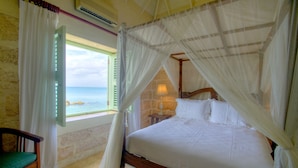 Un dormitorio con cama, una silla, un ventanal con vista al mar y una lámpara.