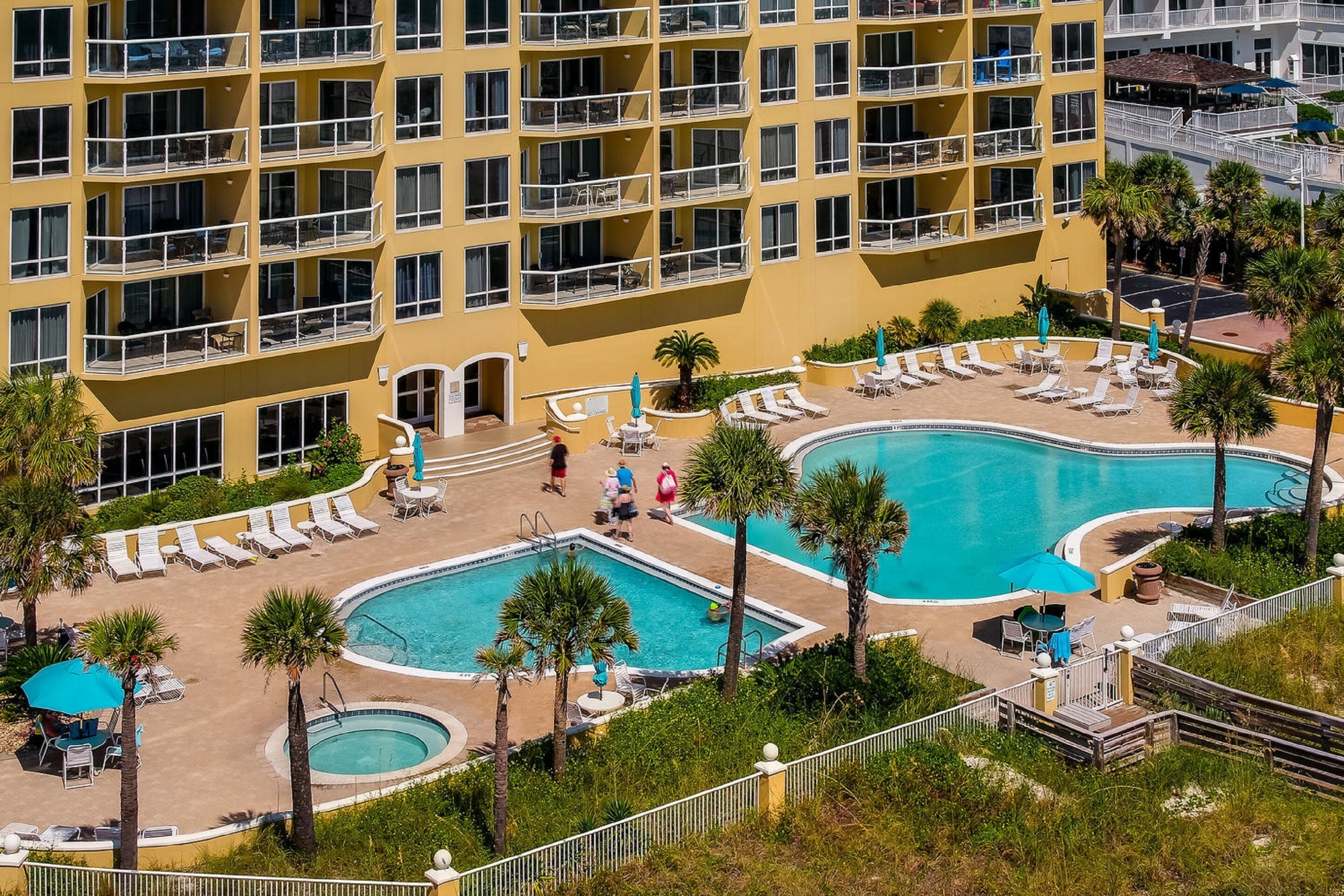 A multi-story hotel with a pool area featuring sun loungers and palm trees.