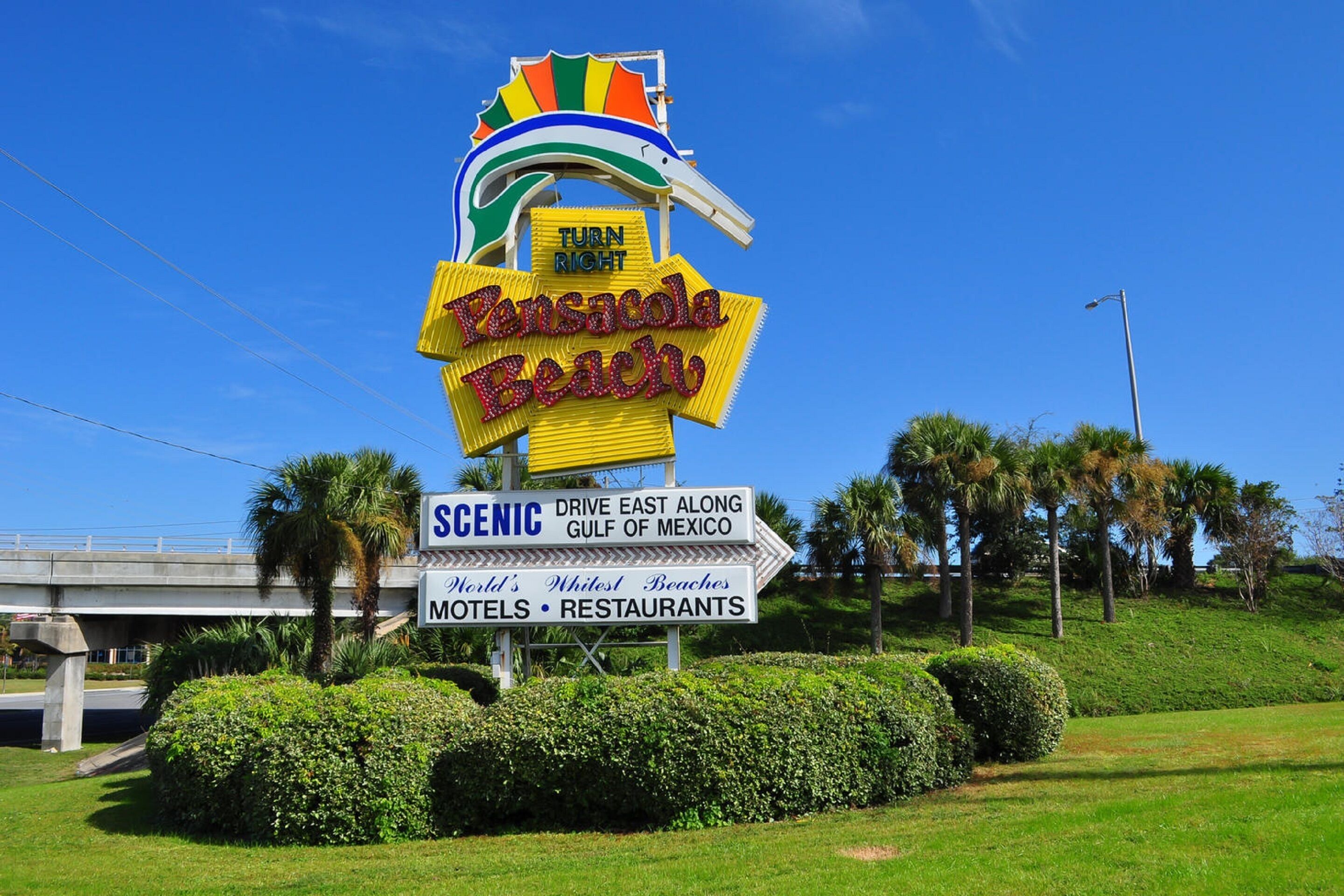 A sign for Pensacola Beach with directions to scenic areas and amenities like hotels and restaurants.