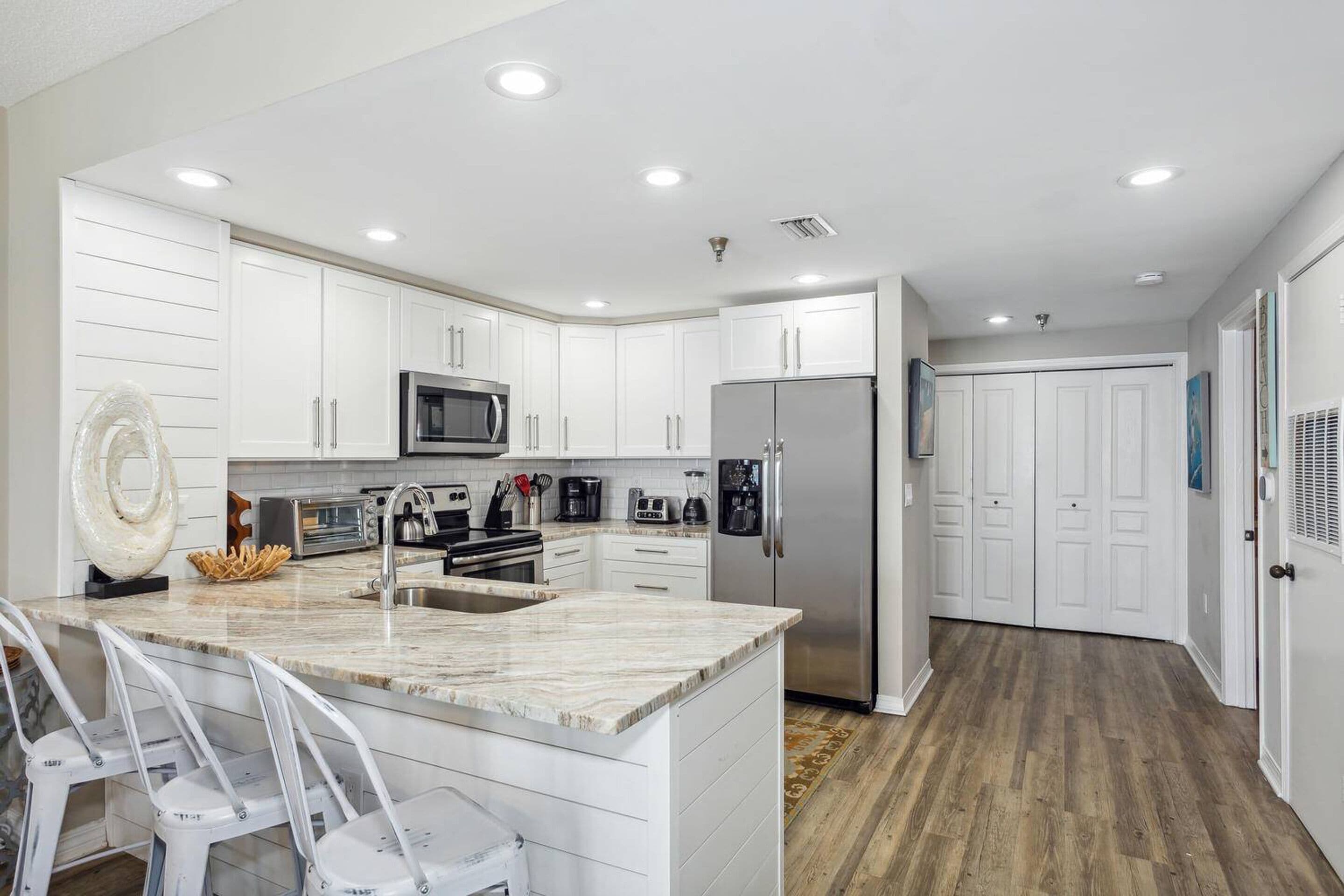 A modern kitchen with white cabinetry, a marble countertop, and stainless steel appliances.