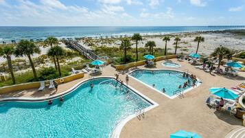 A resort pool area with multiple swimming pools, sun loungers, and umbrellas.