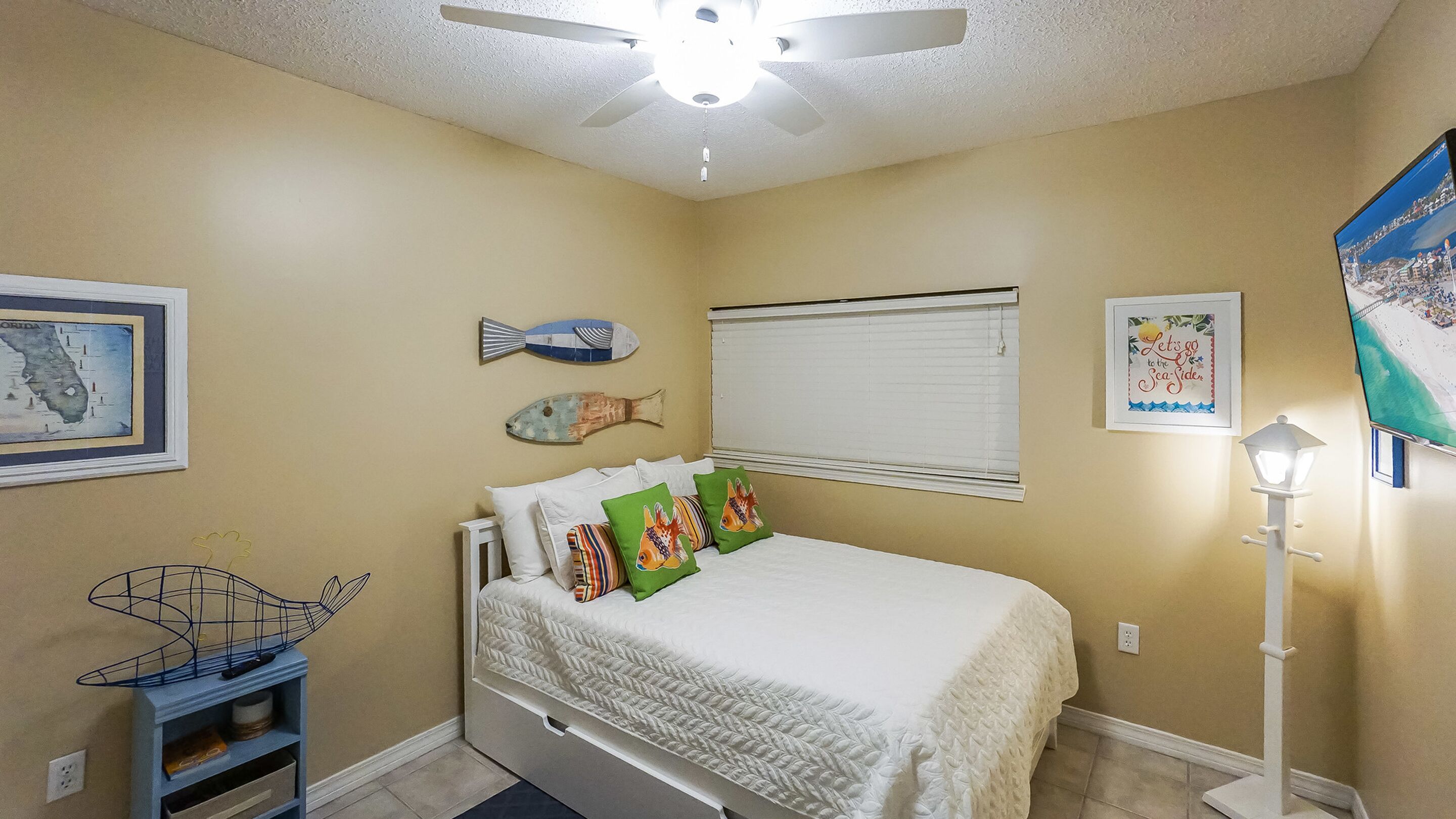 Ein Schlafzimmer mit Bett, Deckenventilator, Fischdeko, einer gerahmten Karte und einer Lampe.