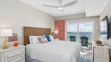 A bedroom with a bed, a nightstand, a ceiling fan, a window with a view, and a chair by the window.