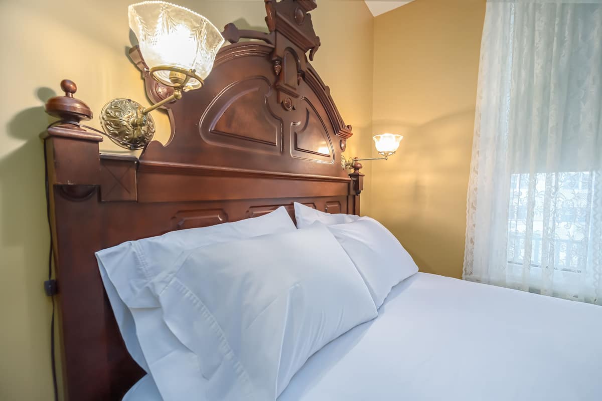 A neatly made bed with white linens, a wooden headboard with intricate carvings, and two wall-mounted sconces.