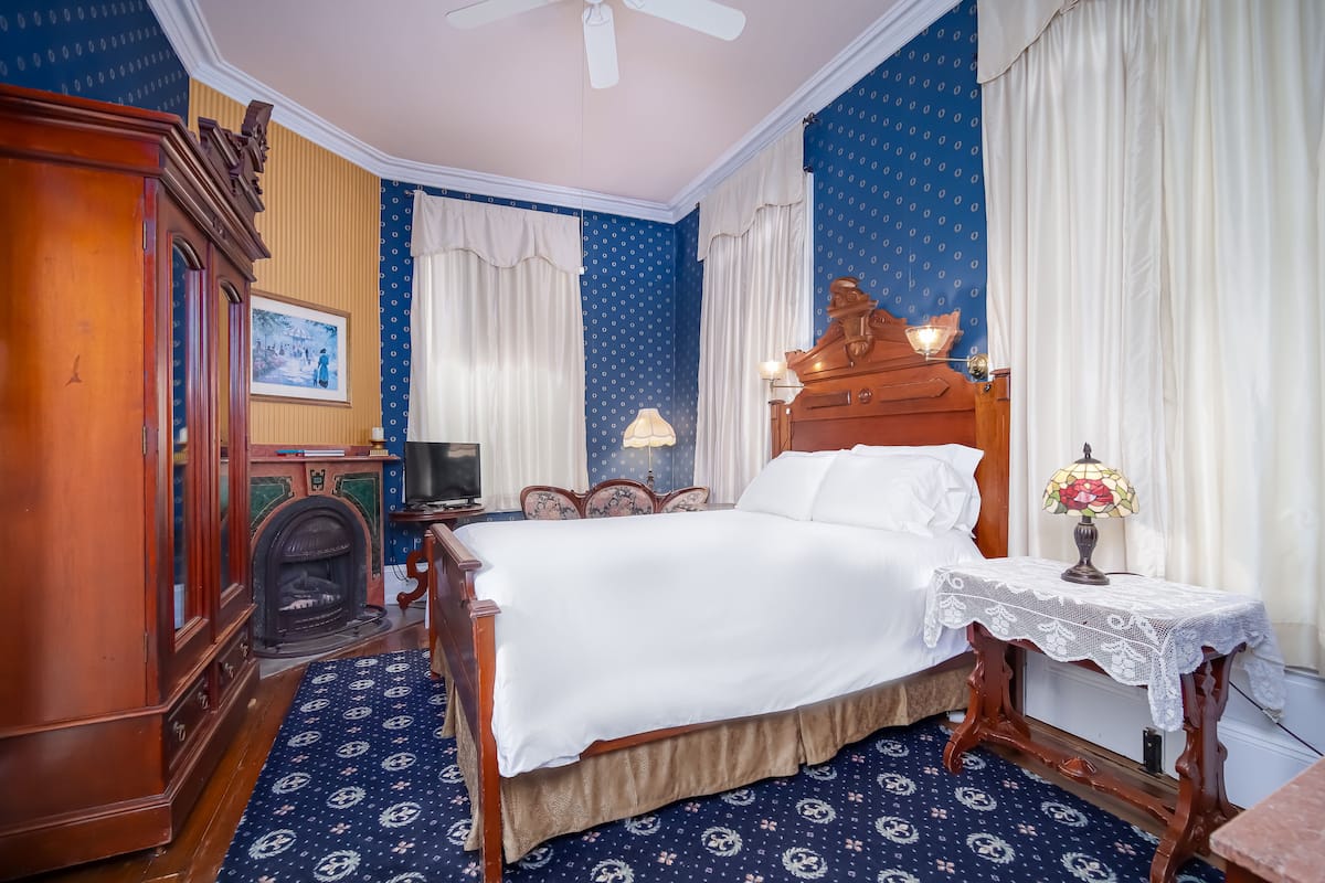 A traditional bedroom with a wooden bed, a nightstand with a lamp, a dresser, and a fireplace.